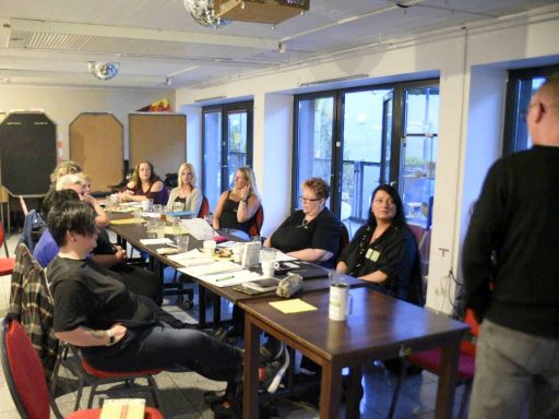 Eine Gruppe von Menschen sitzt an Tischen in einem hellen Raum und diskutiert.