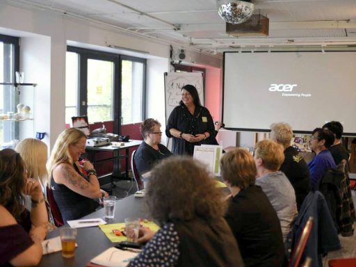 Eine Personen leitet ein Meeting mit einer Gruppe von Teilnehmern in einem Konferenzraum.