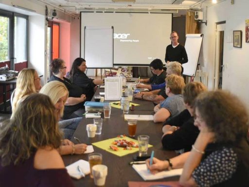 Gruppendiskussion in einem Seminarraum mit Teilnehmern und einer Präsentation.